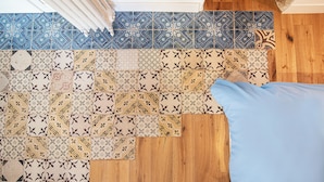 Une pièce avec un plancher en bois, un coussin bleu et différents motifs de carreaux sur les murs.