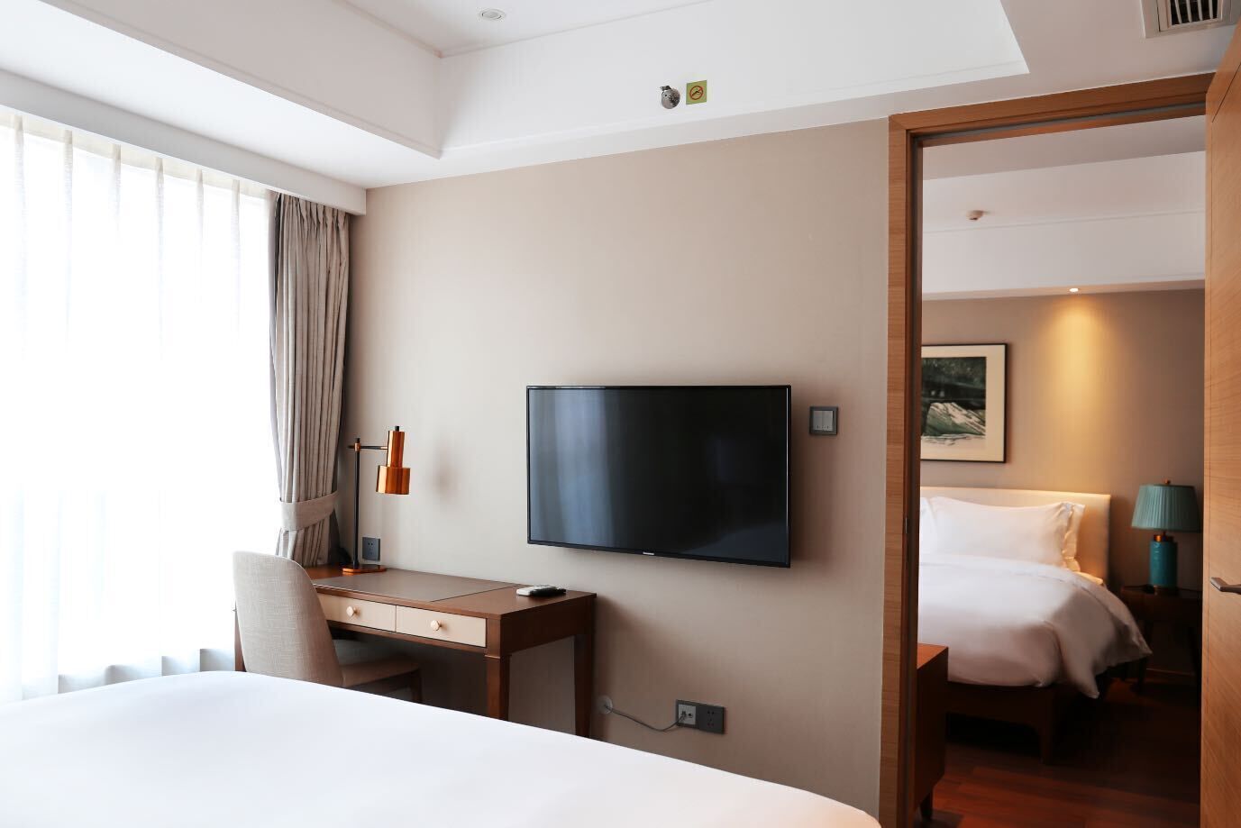 A hotel room with a bed, a desk, a television, and a door leading to another room.