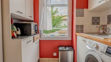 A compact kitchen with a washing machine, a microwave, and a trash bin.