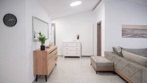 A modern living room with a wooden dresser, a white cabinet, a grey sofa, and a large mirror. - Appartement Sky (Peraia)