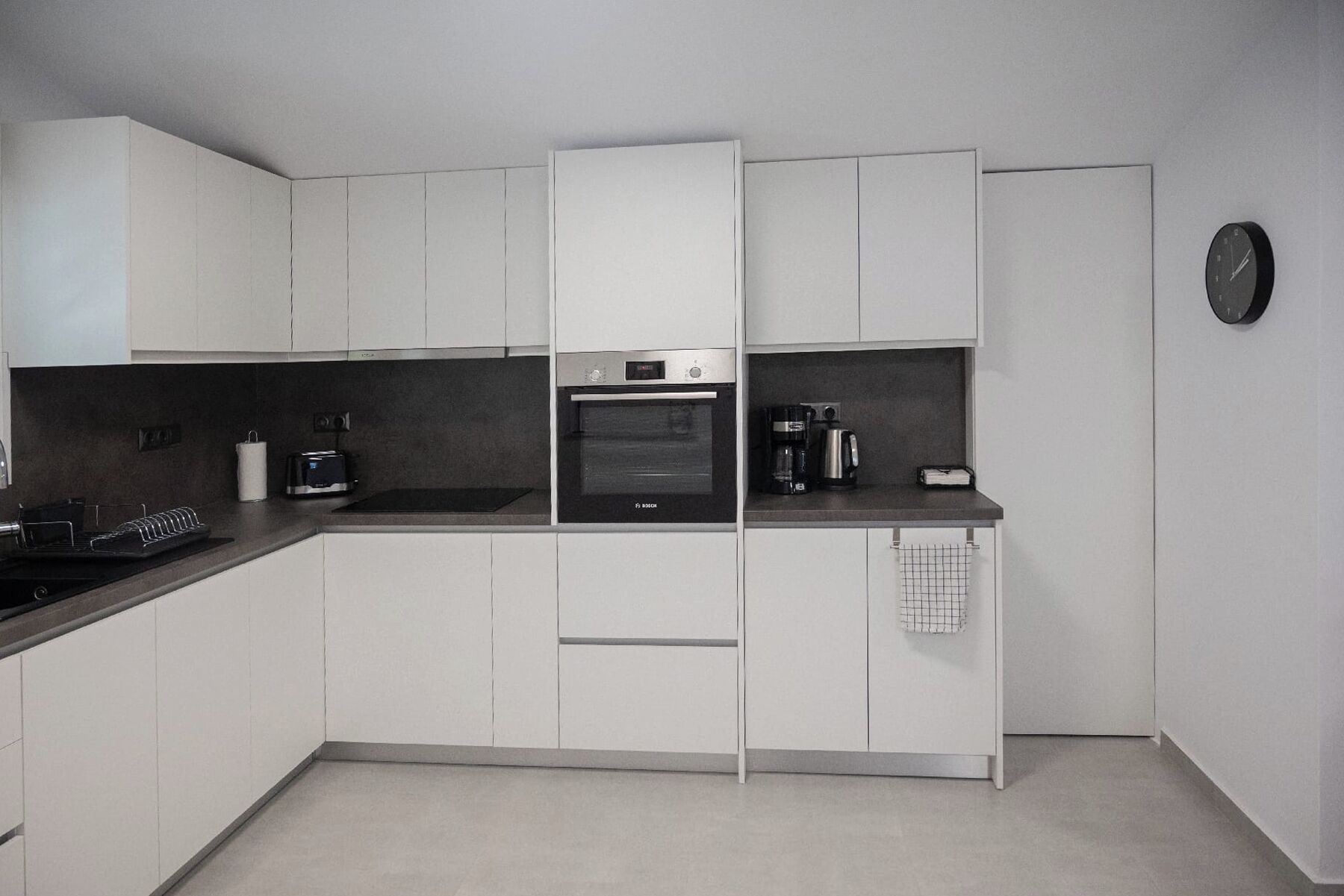 A modern kitchen with white cabinets, a Bosch oven, a coffee maker, and a clock on the wall.