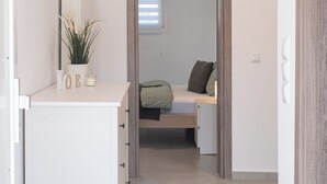 A bedroom with a bed, a bedside table with a plant, and a dresser. - Appartement Sky (Peraia)