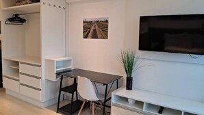 A modern room with a desk, chair, TV, and storage units. - Studio Equipado em Apartamento Clube com Academia no Centro de Curitiba MID Home (Centro Curitiba)