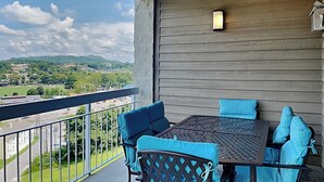 A balcony with a table and chairs, a view of a green landscape and buildings, and a wooden wall.