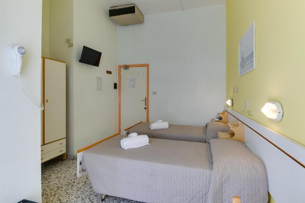 Una camera d'albergo con due letti, una televisione, un asciugacapelli e una porta.