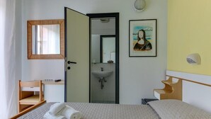 A hotel room with a bed, a desk, a chair, a mirror, a sink, and a framed picture on the wall. - Hotel Villa Merope (Rimini)