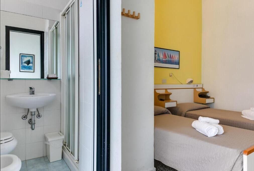 Ein Hotelzimmer mit Bad, inklusive Waschbecken, Toilette und Dusche. Es gibt zwei Betten mit Handtüchern.