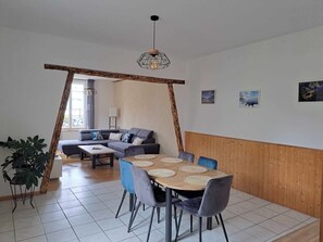 Een moderne woonkamer met een houten eettafel, een grijze bank en een groot raam.