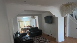 Een woonkamer met een zwarte leren bank, een rug van luipaardprint en een kroonluchter.