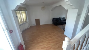 Een ruime woonkamer met houten vloeren, een zwarte leren bank en een kroonluchter.