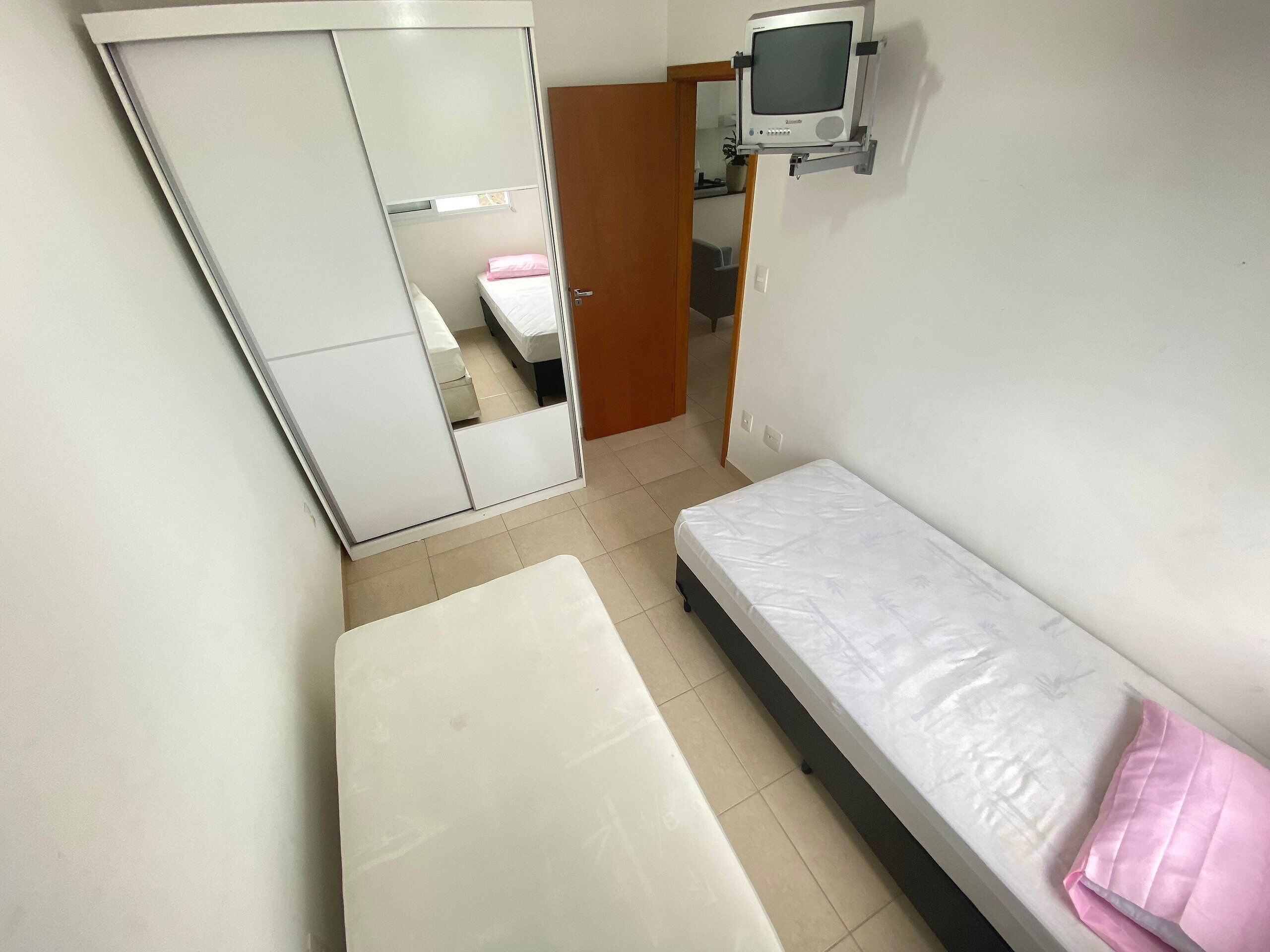 A small, compact room with a bed, a bedside table, and a television mounted on the wall.