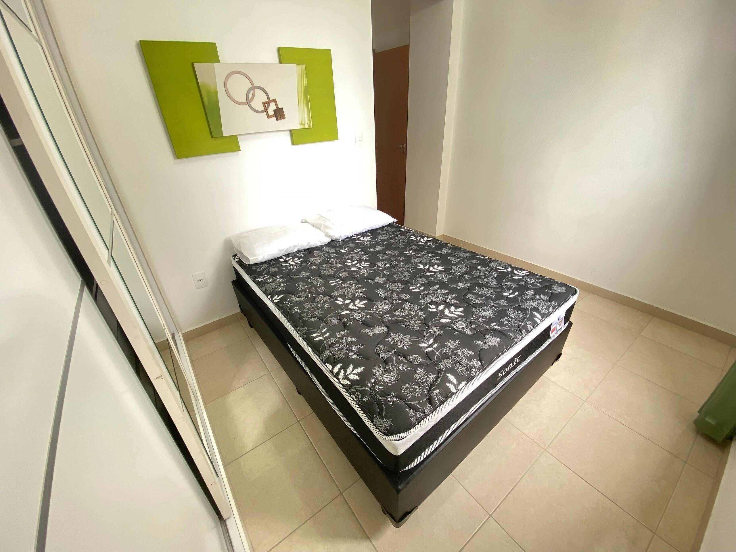 Ein Bett mit einem blumigem Matratzenbezug in einem Zimmer mit weißen Wänden und einer grünen Akzentwand.