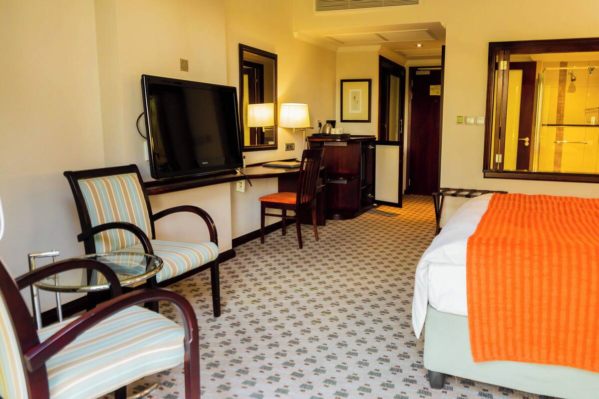 Ein Hotelzimmer mit Bett, Fernseher, Schreibtisch mit Stuhl und einem durchgegangenen Tür erkennbaren Badezimmer.