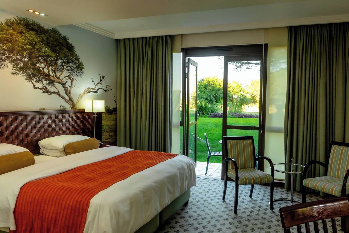 Ein Hotelzimmer mit einem großen Bett, einem Fernseher, einem Schreibtisch und Blick auf einen Garten durch eine Schiebetür.