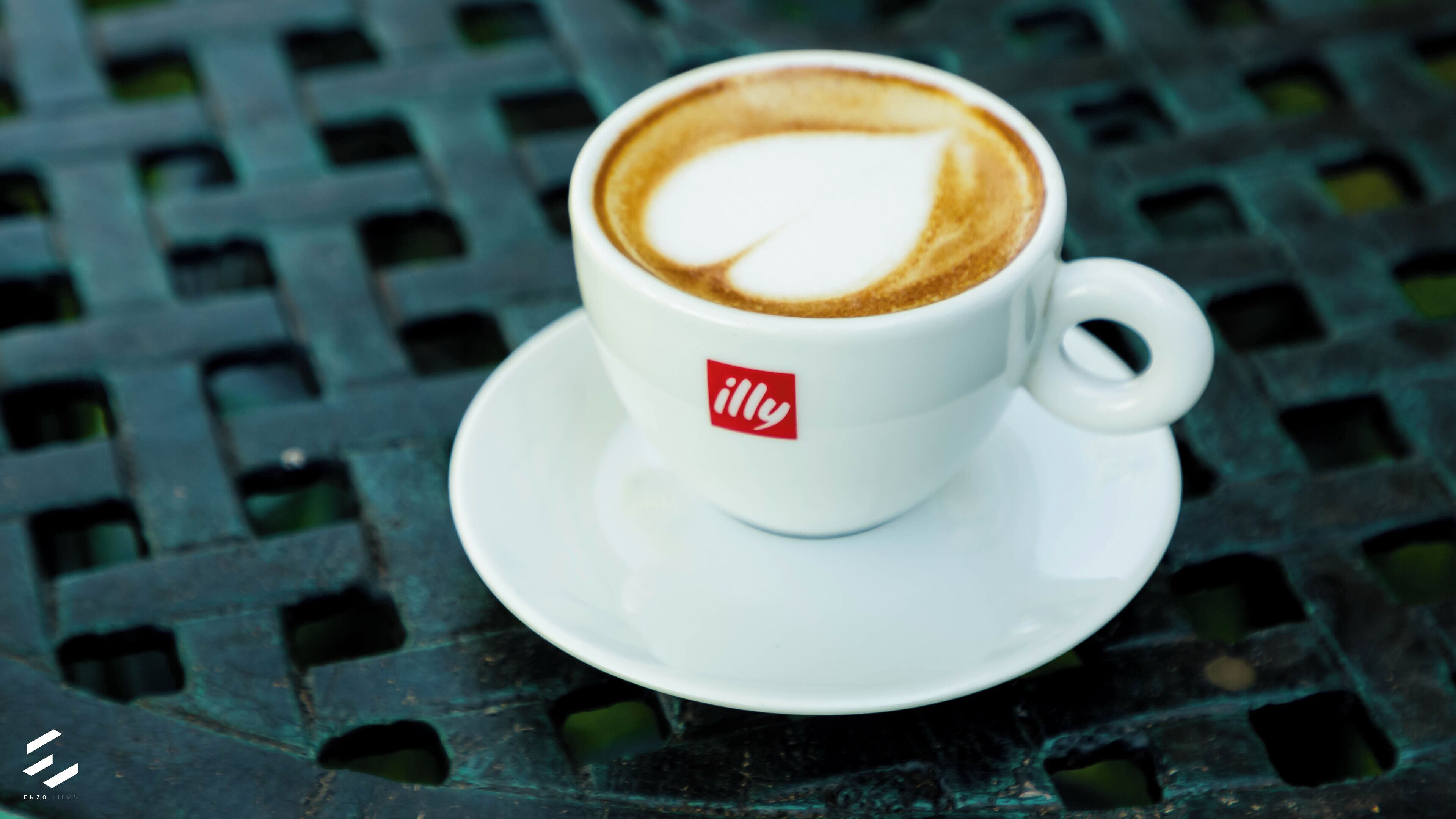 A white cup with a heart-shaped latte art on a green metal table.