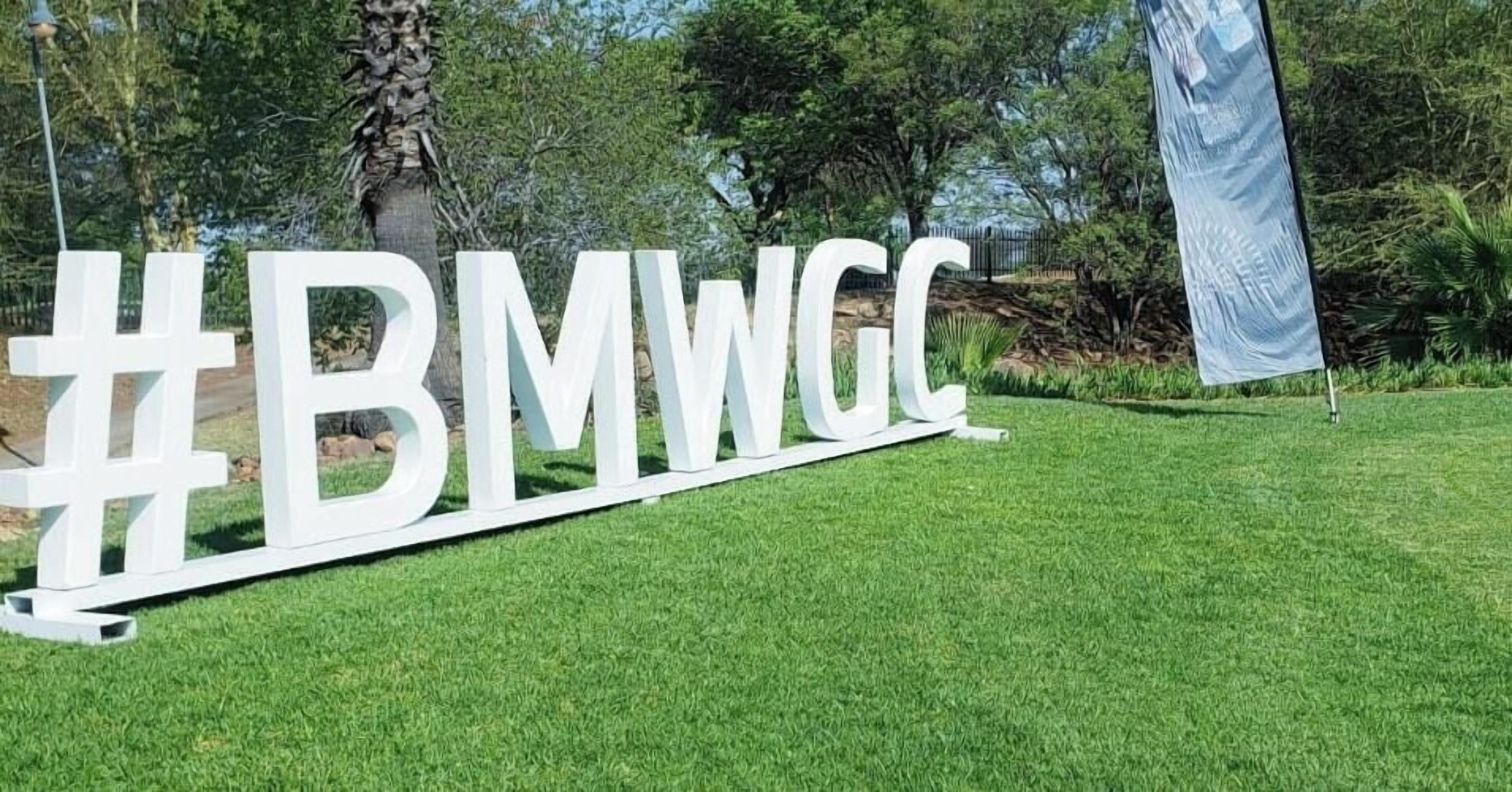 A large white sign with the text "#BMWWGC" on a grassy area.