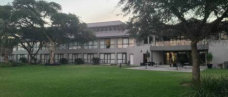 Un edificio moderno con techo plano, ventanas grandes y un patio con césped y zona de estar.