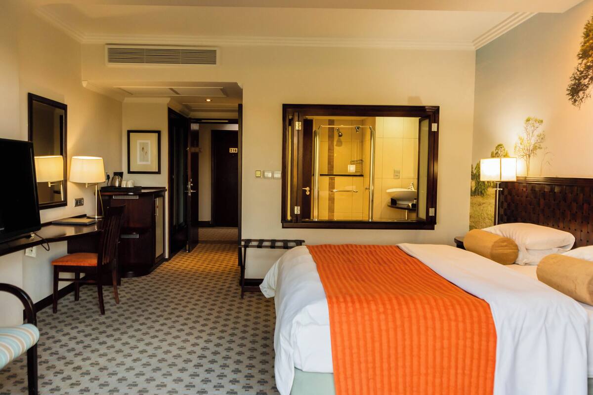Ein Hotelzimmer mit Bett, Schreibtisch, Fernseher und einem durch einen Spiegel einsehbaren Badezimmer.