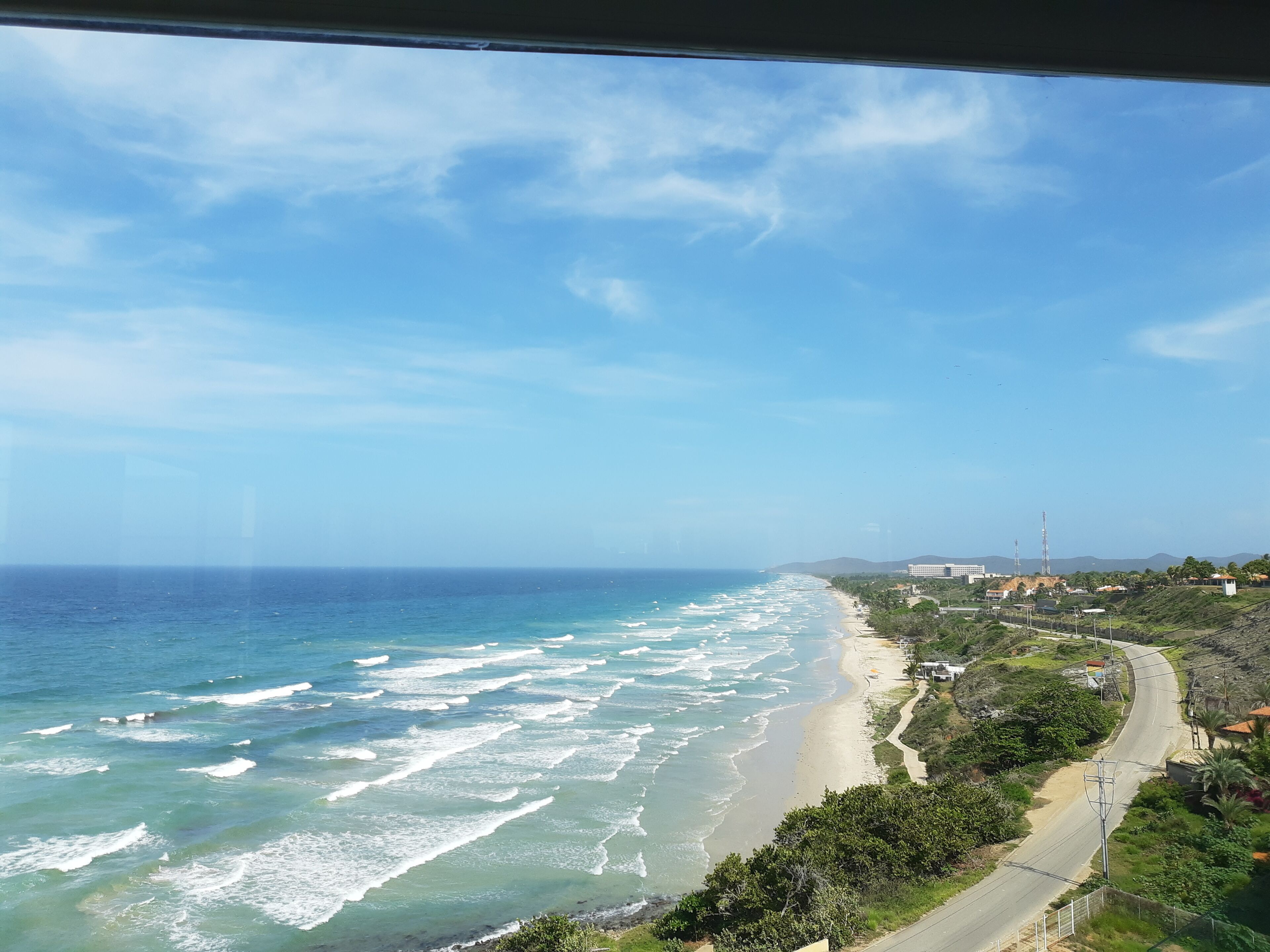 Vista costera con playa, olas del océano y una carretera que serpentea por la orilla.