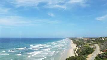 Vista costera con playa, olas del océano y una carretera que serpentea por la orilla.