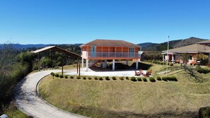 Una casa de dos pisos con un porche cubierto y vistas de las colinas circundantes.