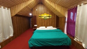 A room with a sloped ceiling, wooden walls, a bed with a teal bedspread, and a red carpet.