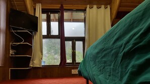 A room with a bed, a TV mounted on the wall, a window with curtains, and a red carpeted floor.