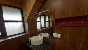 A wooden cabin bathroom with a round sink, a mirror, a window, and a red storage shelf.