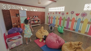Een speelkamer met een bakstenen muur, houten planken en kleurrijke decoraties, waaronder een hek en bloemen.