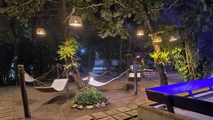 Een terras 's nachts met hangmatten, sfeerverlichting en een blauwe bank.
