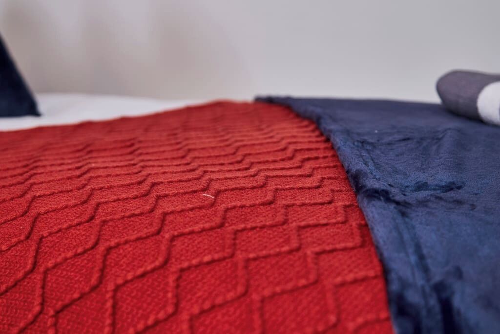 Primer plano de una manta roja con textura y una manta azul oscuro sobre una cama.
