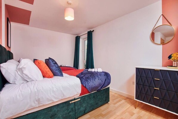 A bedroom with a bed, a dresser, a mirror, and a window with curtains.