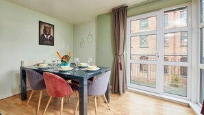 Un coin repas avec une table dressée pour quatre personnes, une œuvre d’art sur le thème des ours accrochée au mur et une grande fenêtre donnant sur un bâtiment en briques.