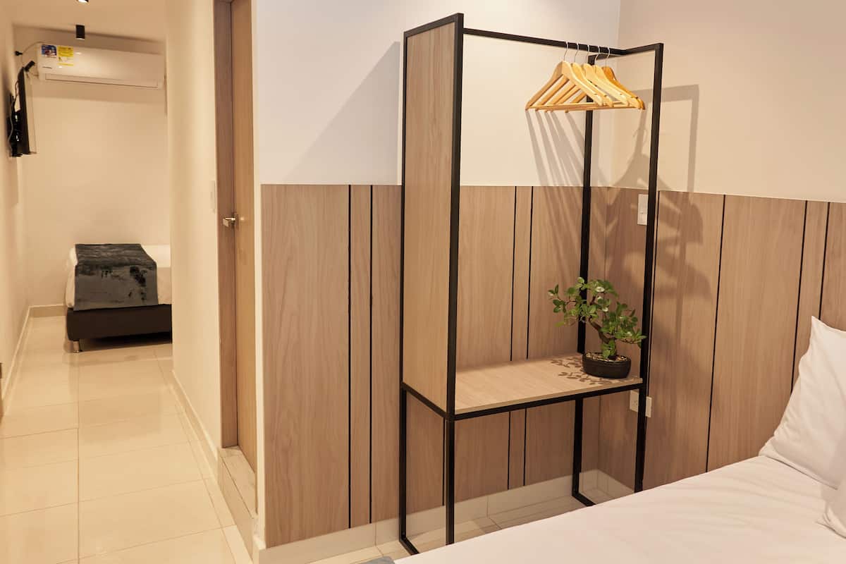 A hotel room with a bed, a wooden wardrobe, a small table with a plant, and a clothing rack.