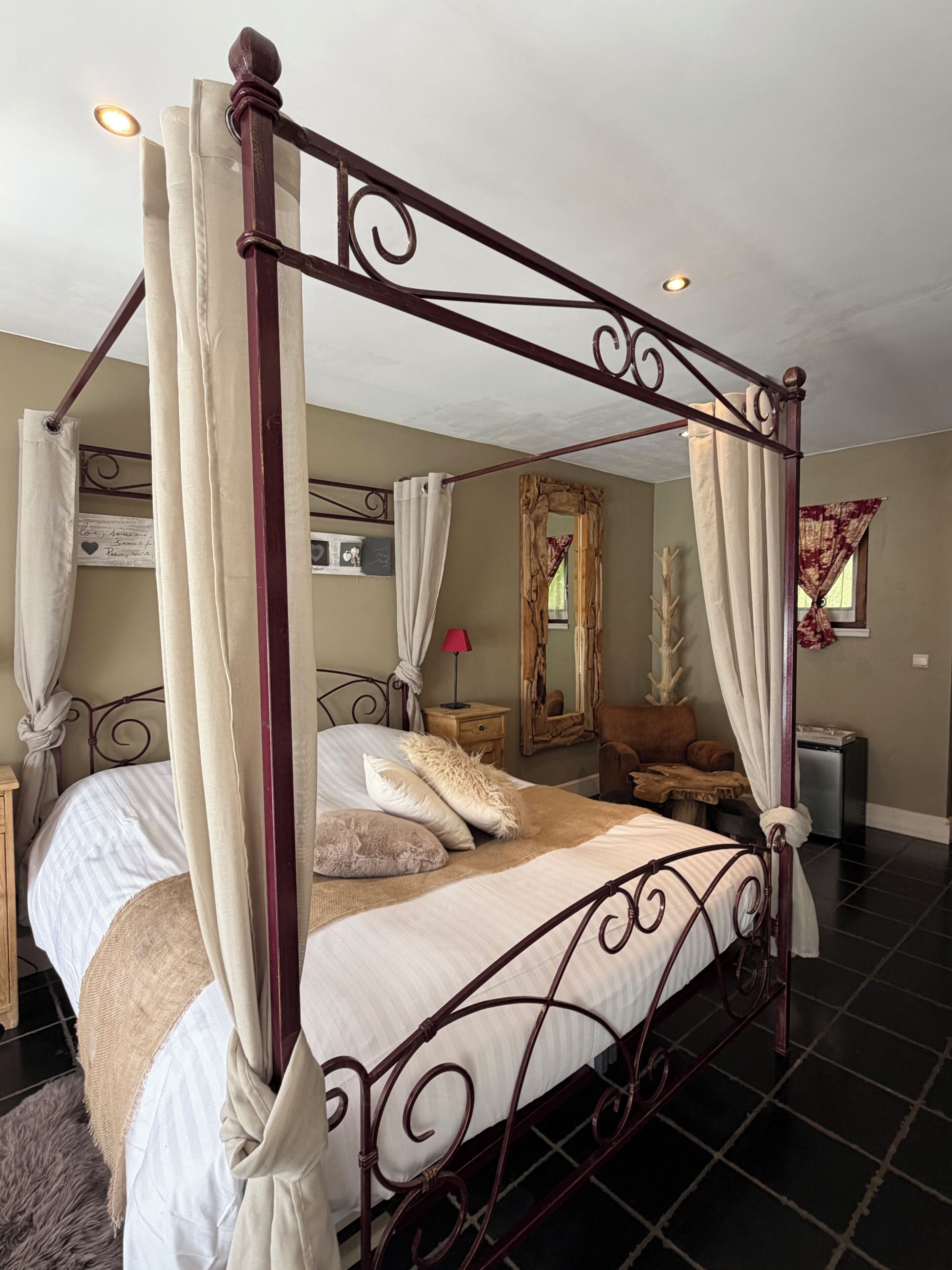 A four-poster bed with a canopy, a bedside table, a mirror, and a small nightstand.