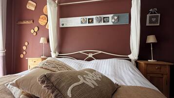 A four-poster canopy bed with a textured throw blanket and pillows, a bedside table with a lamp, and wall decor including wooden plaques and heart-shaped frames.