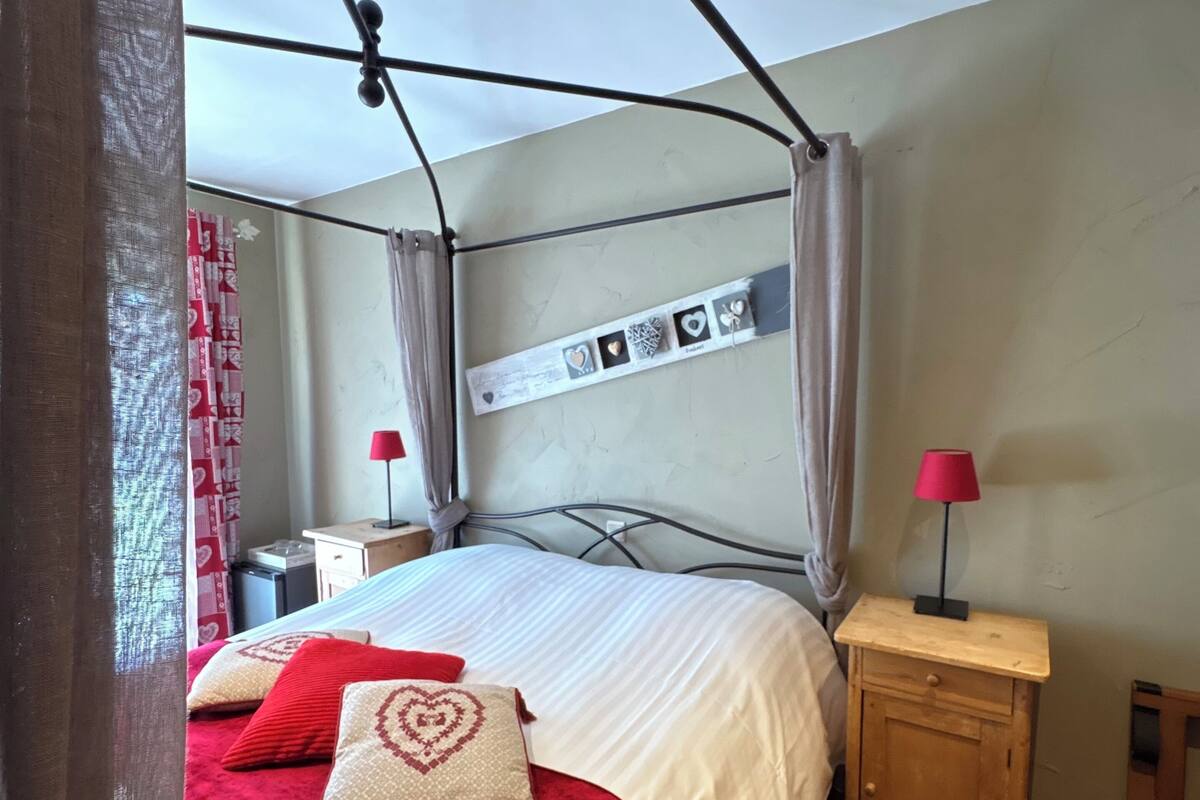 Un dormitorio con cama con dosel, una mesita de noche con lámpara y un estante en la pared con objetos decorativos.