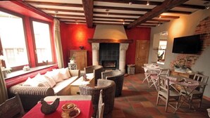 A cozy living room with a fireplace, wicker furniture, and a dining area with a table set for two. - Comme à la ferme (Durbuy)
