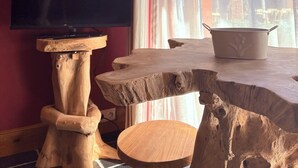 A room with a television on a wooden stand, a window with curtains, and a rustic wooden table. - Comme à la ferme (Durbuy)