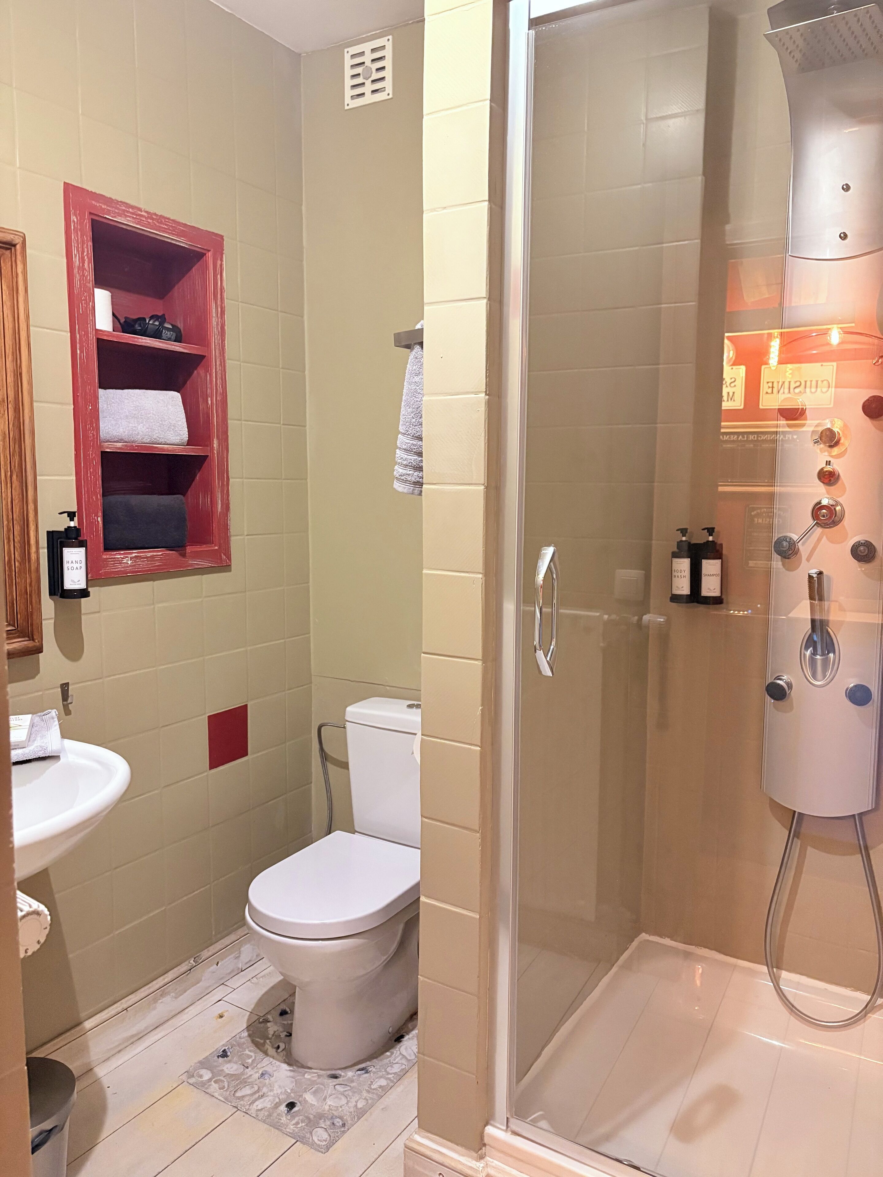Ein Badezimmer mit Toilette, Waschbecken, einer Duschkabine und einem Ablagefach mit Handtüchern und Pflegeprodukten.