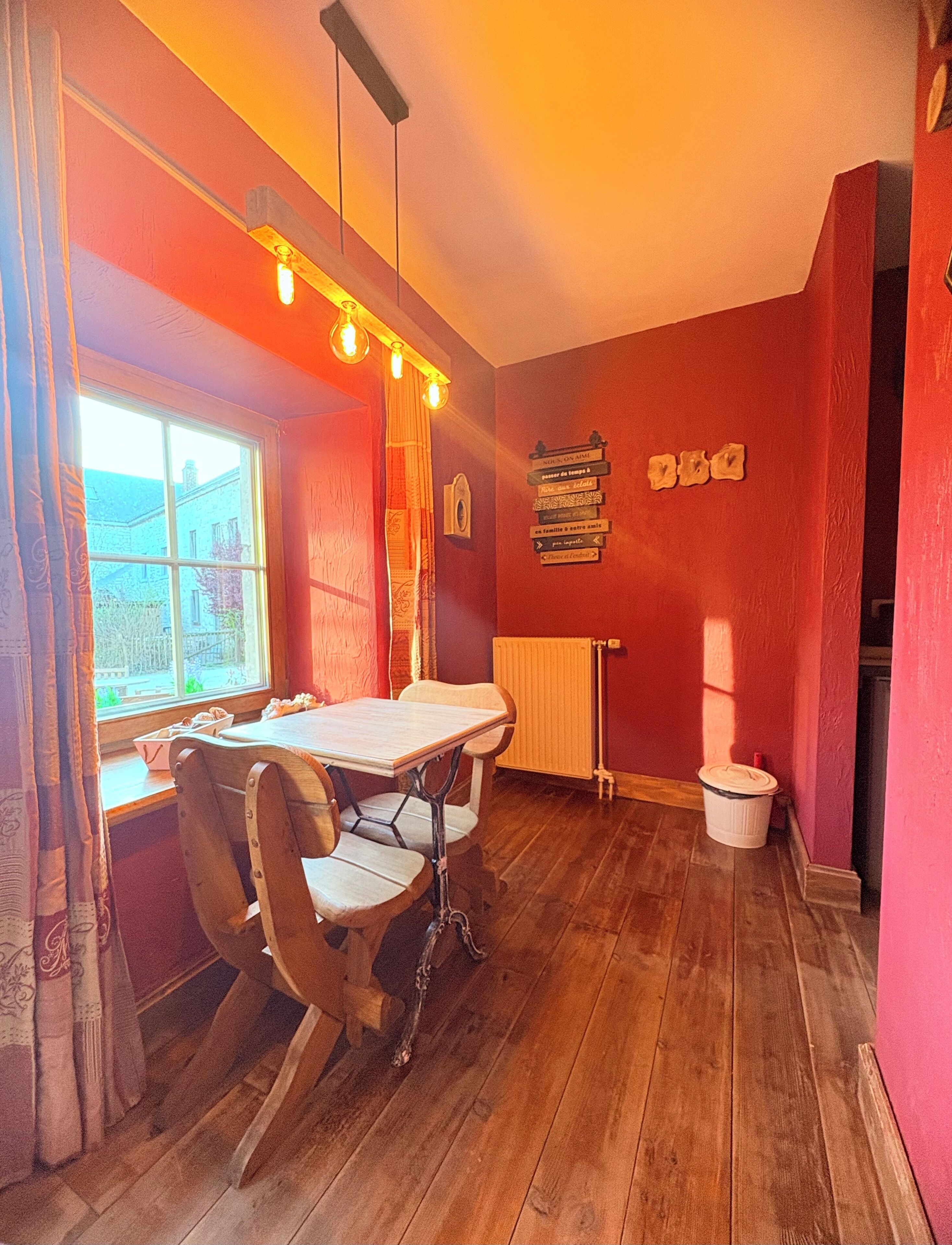 Un comedor con una mesa y sillas de madera, una ventana con cortinas, un radiador y una pared con elementos decorativos.