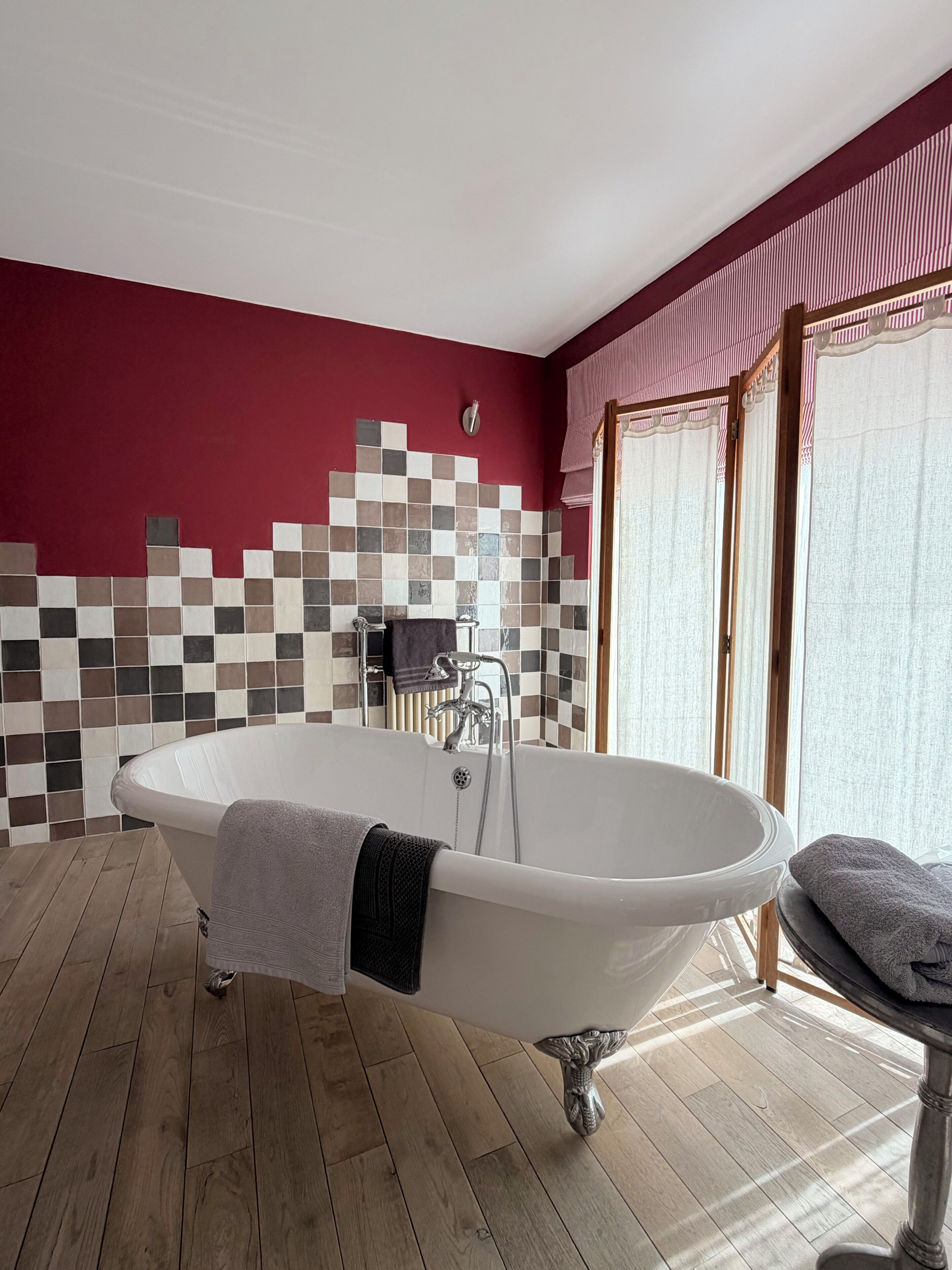 A bathroom with a freestanding bathtub, a tiled wall, and a wooden floor.