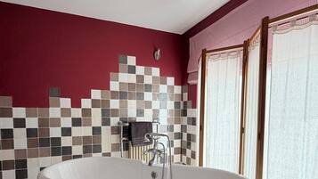A bathroom with a freestanding bathtub, a tiled wall, and a wooden floor.
