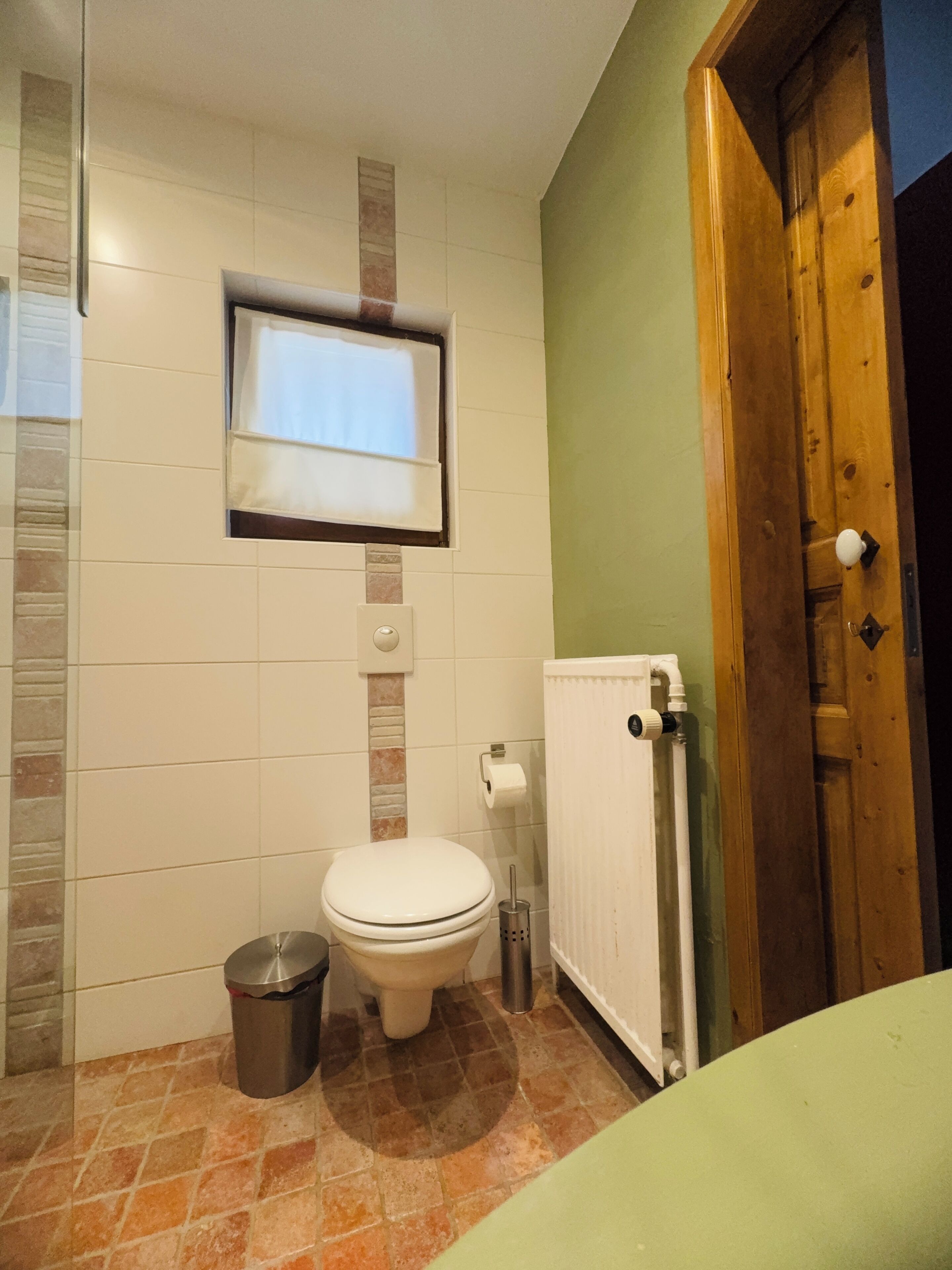 Een badkamer met een toilet, een prullenbak, een handdoekhouder en een raam.