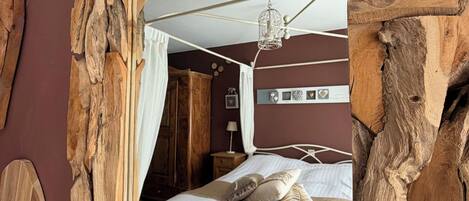 A bedroom with a wooden-framed mirror, a bed with white bedding, a hanging light fixture, and a wooden headboard.