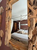Un dormitorio con espejo de madera, cama con ropa de cama blanca, lámpara colgante y cabecero de madera.