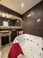 A modern bathroom with a freestanding bathtub, a vanity with a bowl sink, and dark tiled walls.