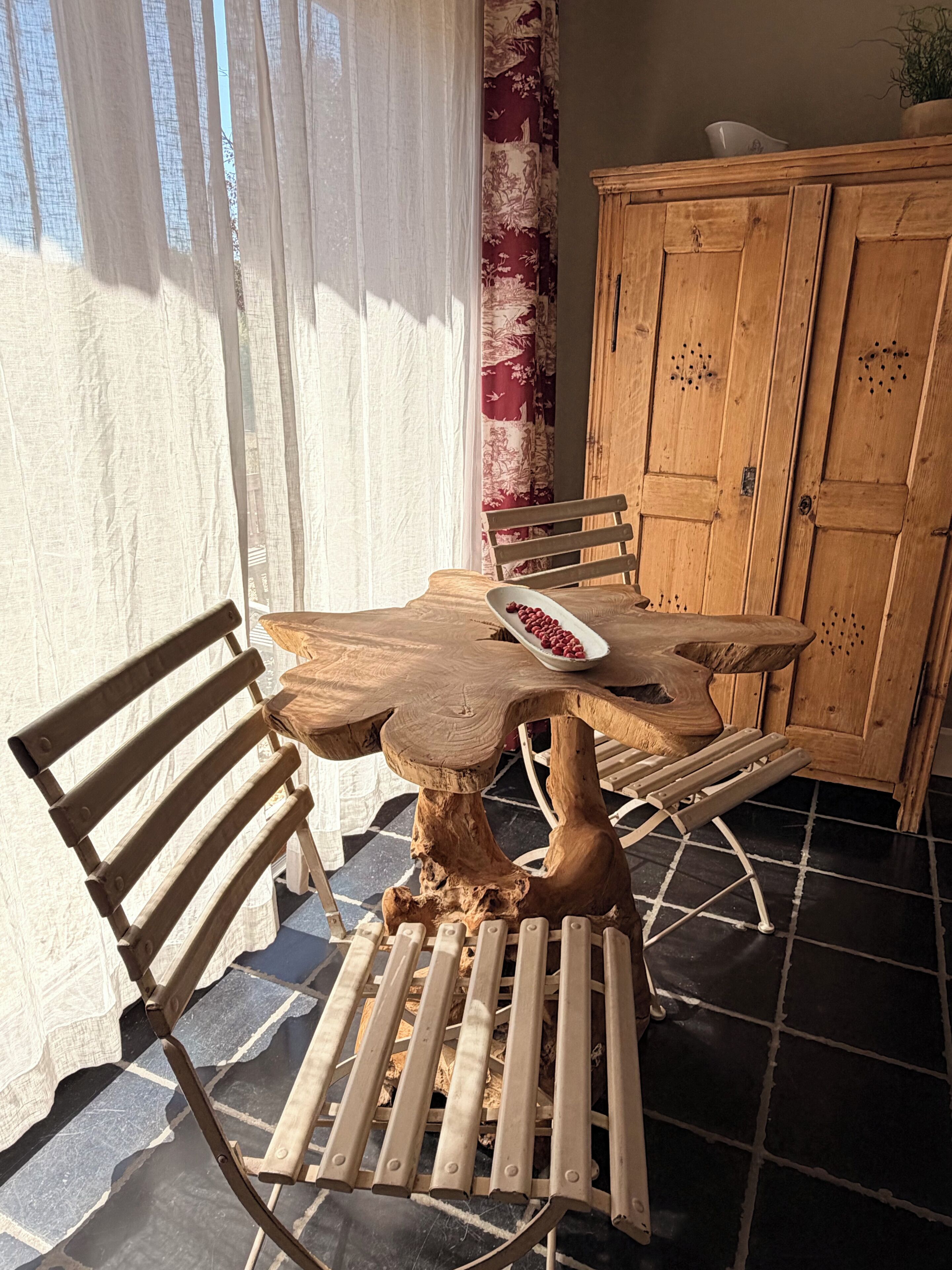Een houten eettafel met stoelen, een kast en een raam met gordijnen.