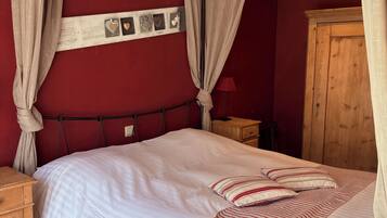 Un dormitorio con una cama, cortinas, una mesita de noche, un armario de madera y una pared decorada con cuadros.