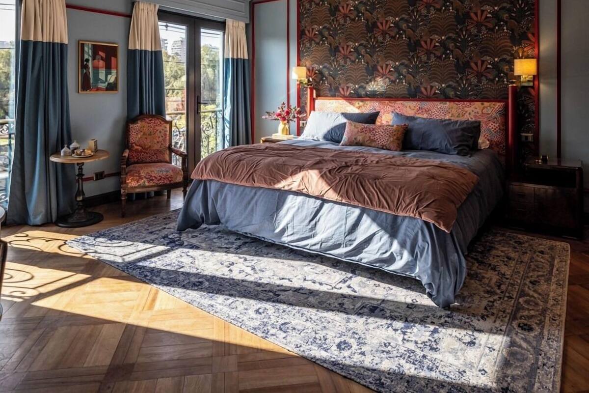 Une chambre avec un grand lit, une chaise, une table et un mur décoré de motifs.